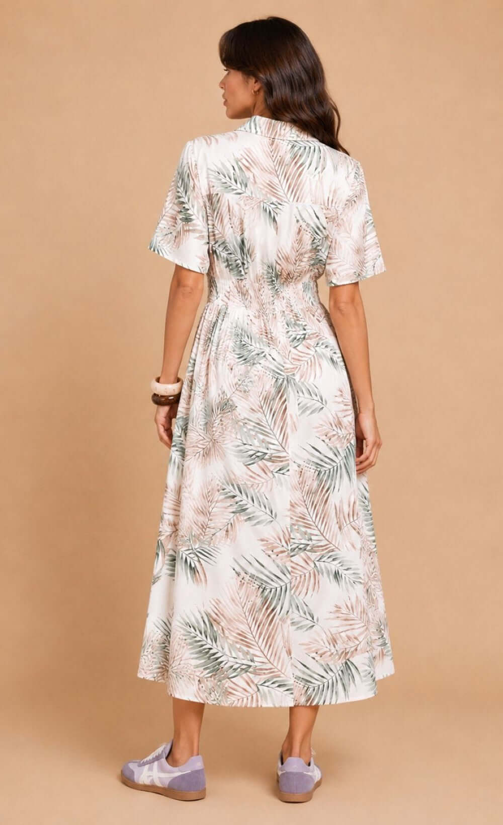 Back view of a trendy chic UK woman wearing a palm print midi dress with a relaxed silhouette and button-down detail.