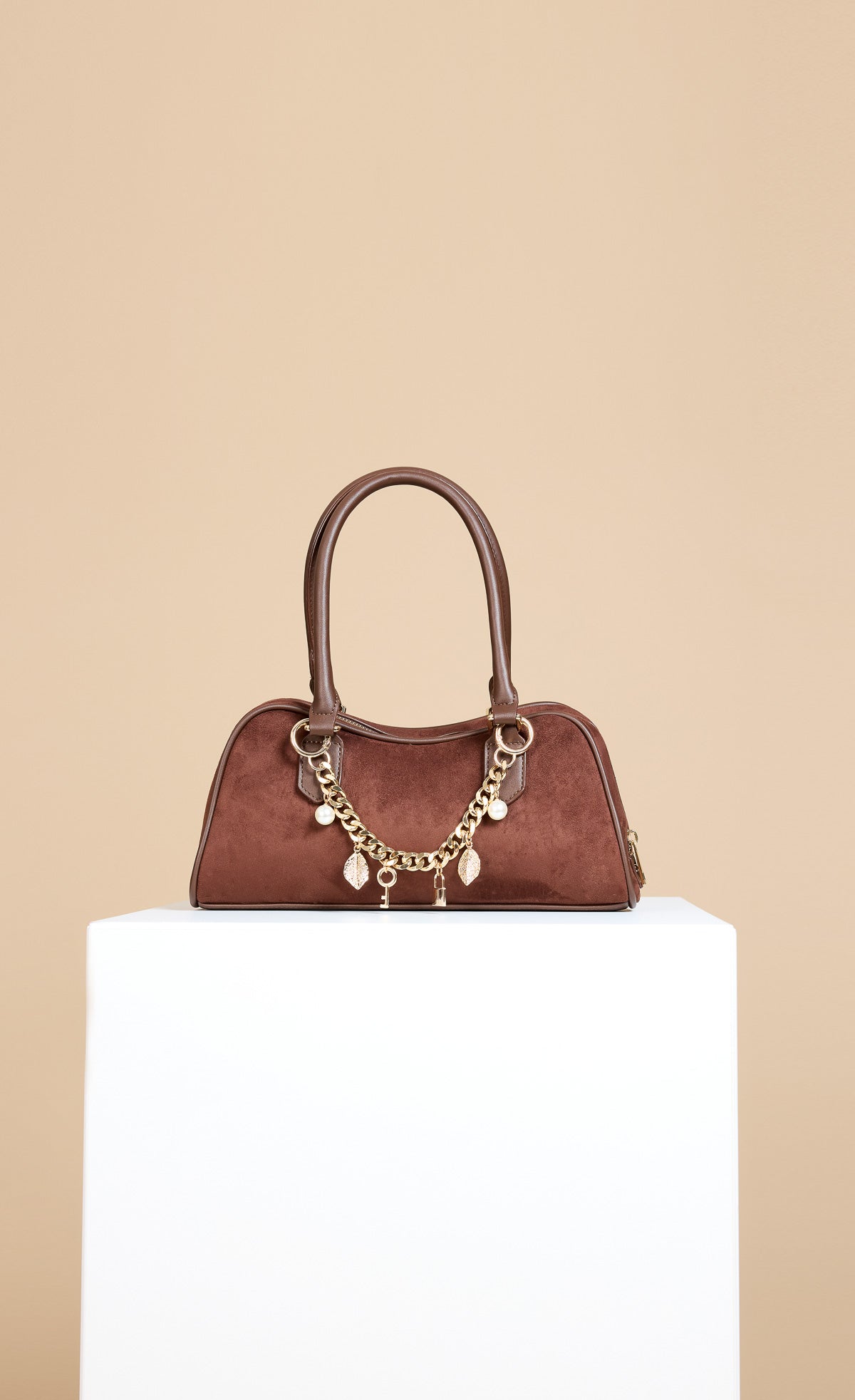 Chocolate Faux Suede Shoulder Bag with gold chain and charm detail on a white pedestal