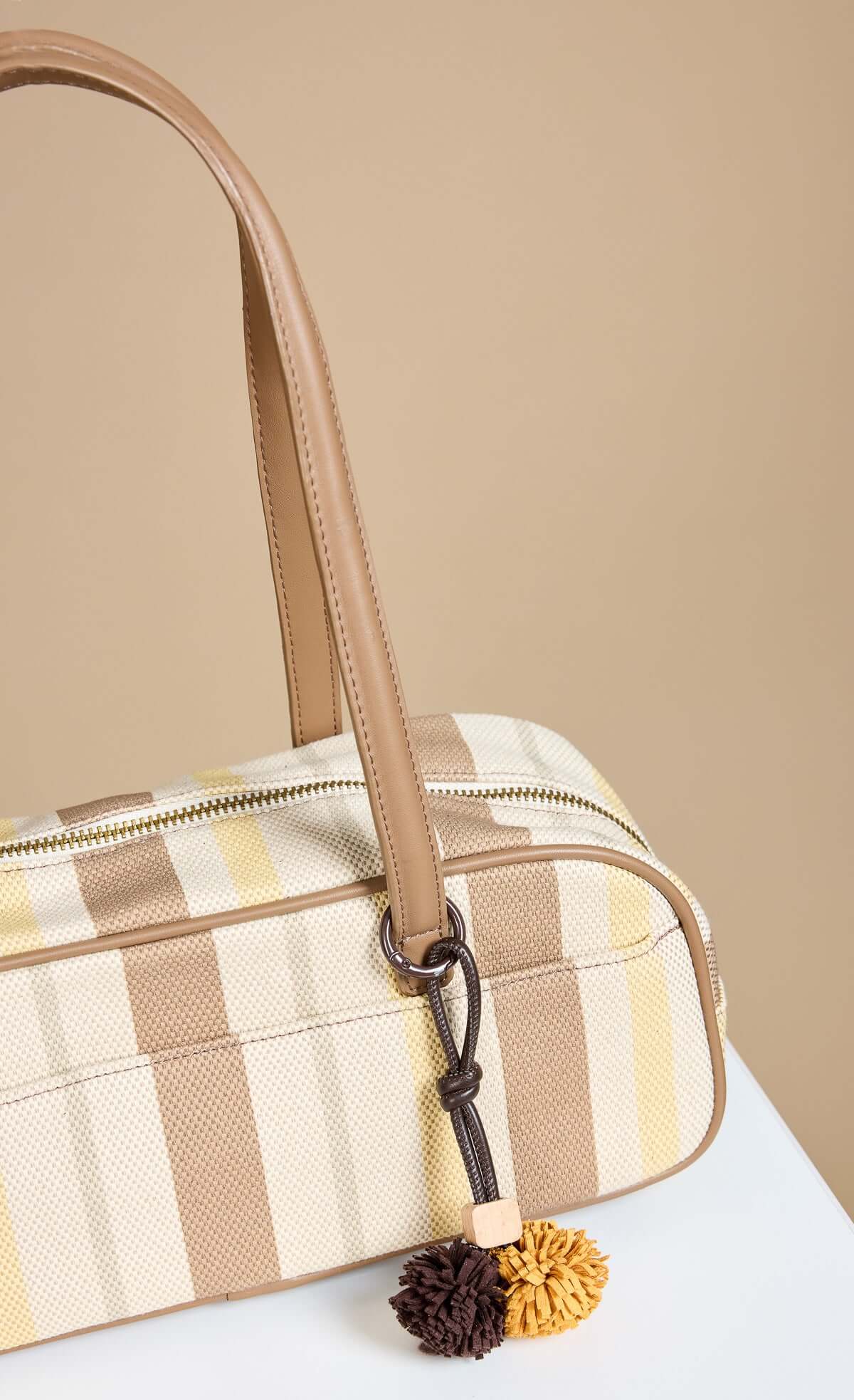 Mocha Lemon Stripe Elongated Shoulder Bag featuring textured fabric and faux leather straps with pom pom charm detail.