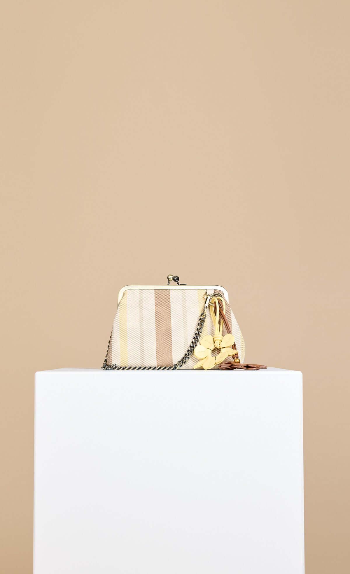 Mocha Lemon Stripe Metal Frame Shoulder Bag with chain strap and flower charm displayed on a pedestal.