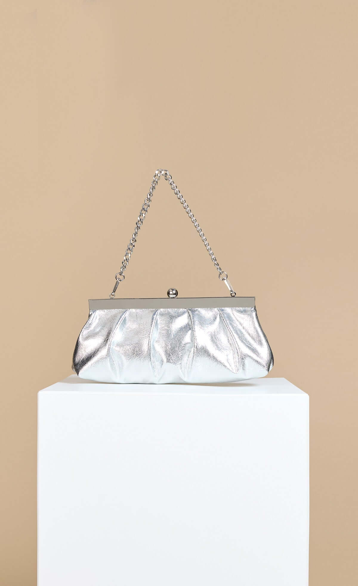 Metallic Silver Elongated Clutch Bag with detachable chain shoulder strap displayed on a pedestal.