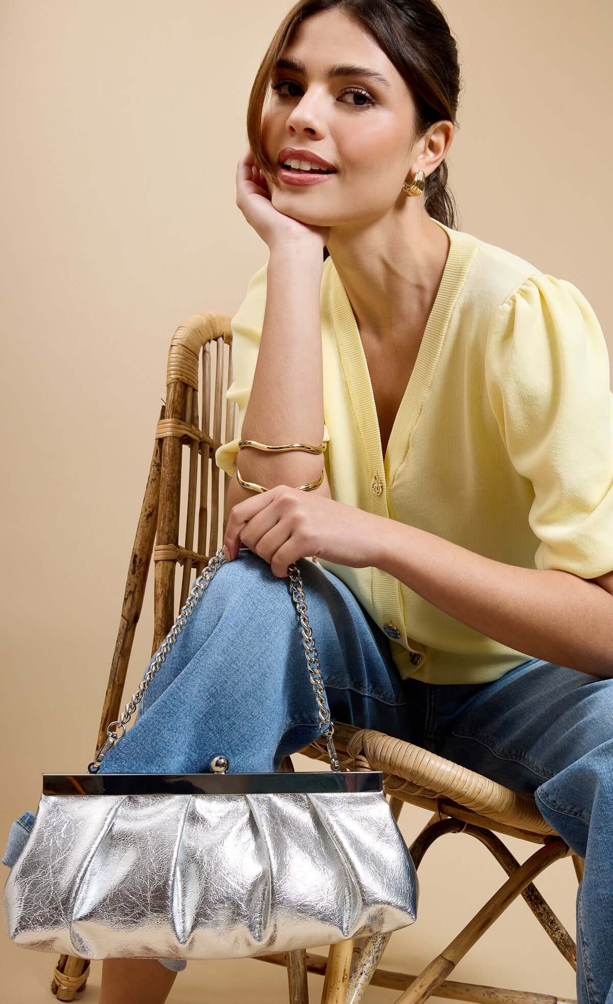 Model showcasing a Metallic Silver Elongated Clutch Bag with chain strap, wearing a yellow top and blue jeans.
