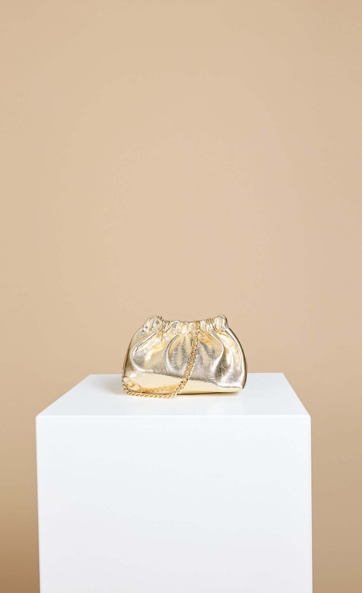Valencia Metallic Gold Ruched Top Shoulder Bag displayed on a white pedestal, showcasing its chain strap.