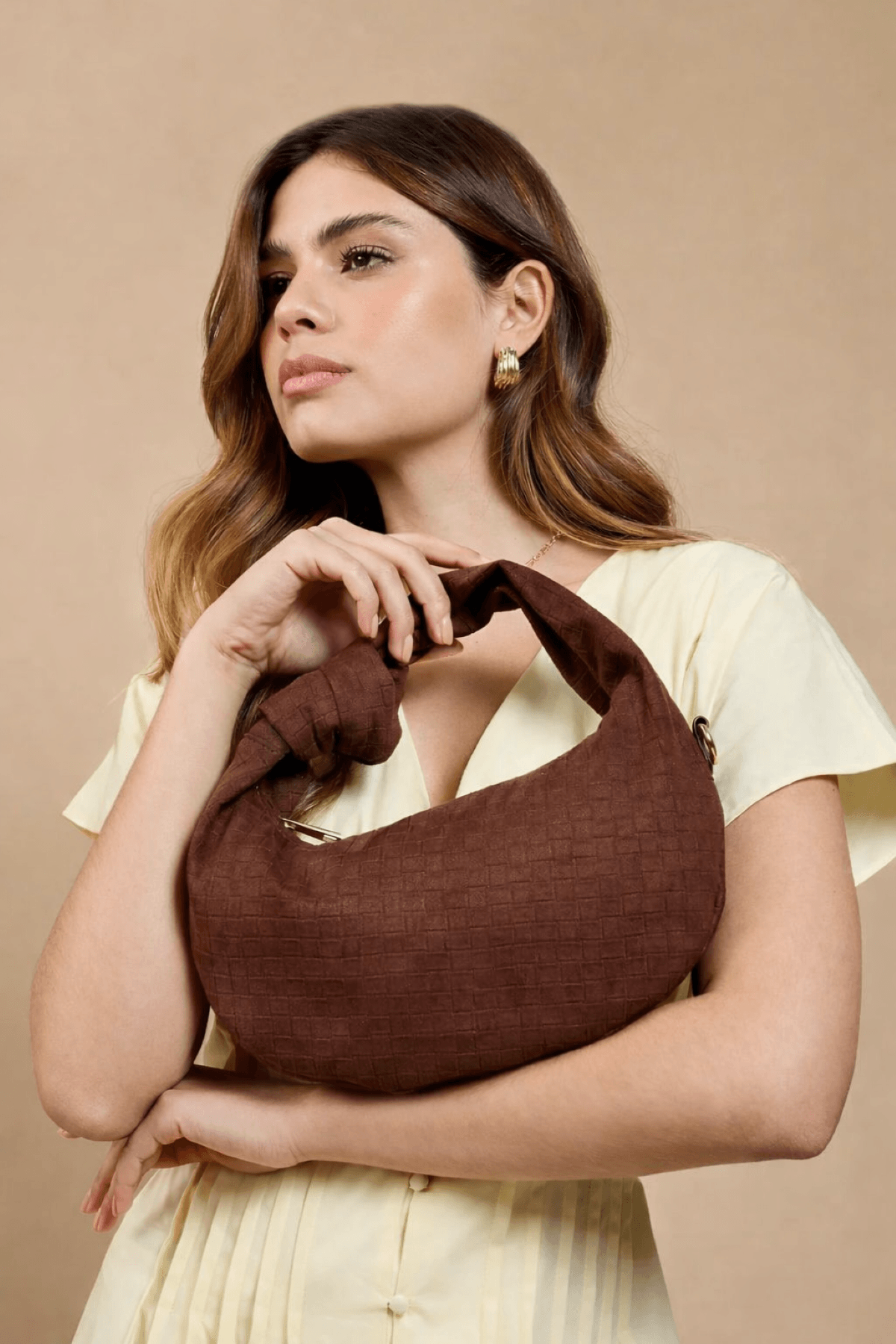 Chocolate Faux Suede Woven Emboss Grab Bag held by a model, featuring knot handle and embossed pattern.