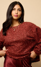 Mireille Cherry Sequin Eyelash Jumper in a cozy red hue, featuring sequins and a relaxed fit, styled with a satin skirt.