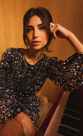 Model wearing a Tatienne Black Velvet and Silver Sequin Mini Dress, striking a pose near a piano.