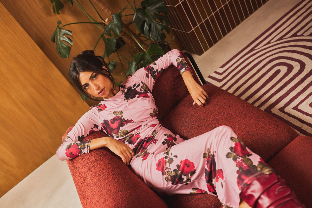 Model wearing the pink floral Marlene dress reclining on a red sofa